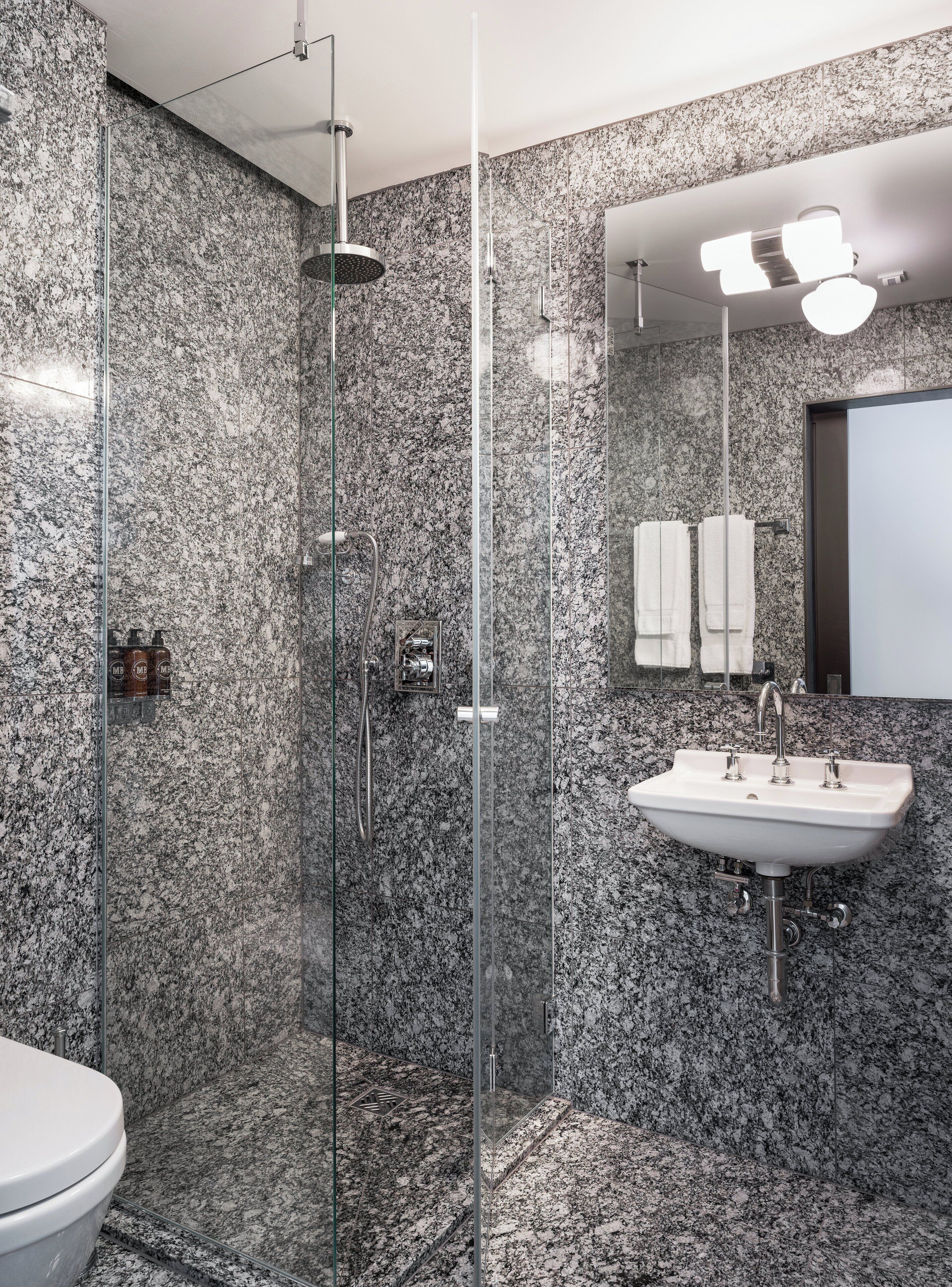 Un baño moderno con ducha de vidrio, un lavamanos blanco y una pared revestida de mármol.