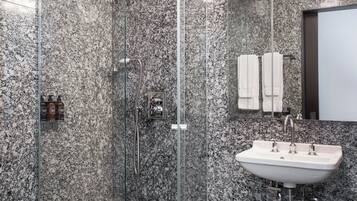 Un baño moderno con ducha de vidrio, un lavamanos blanco y una pared revestida de mármol.