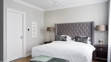 A bedroom with a tufted headboard, a large bed with white linens, two bedside tables with lamps, a bench, and a door.