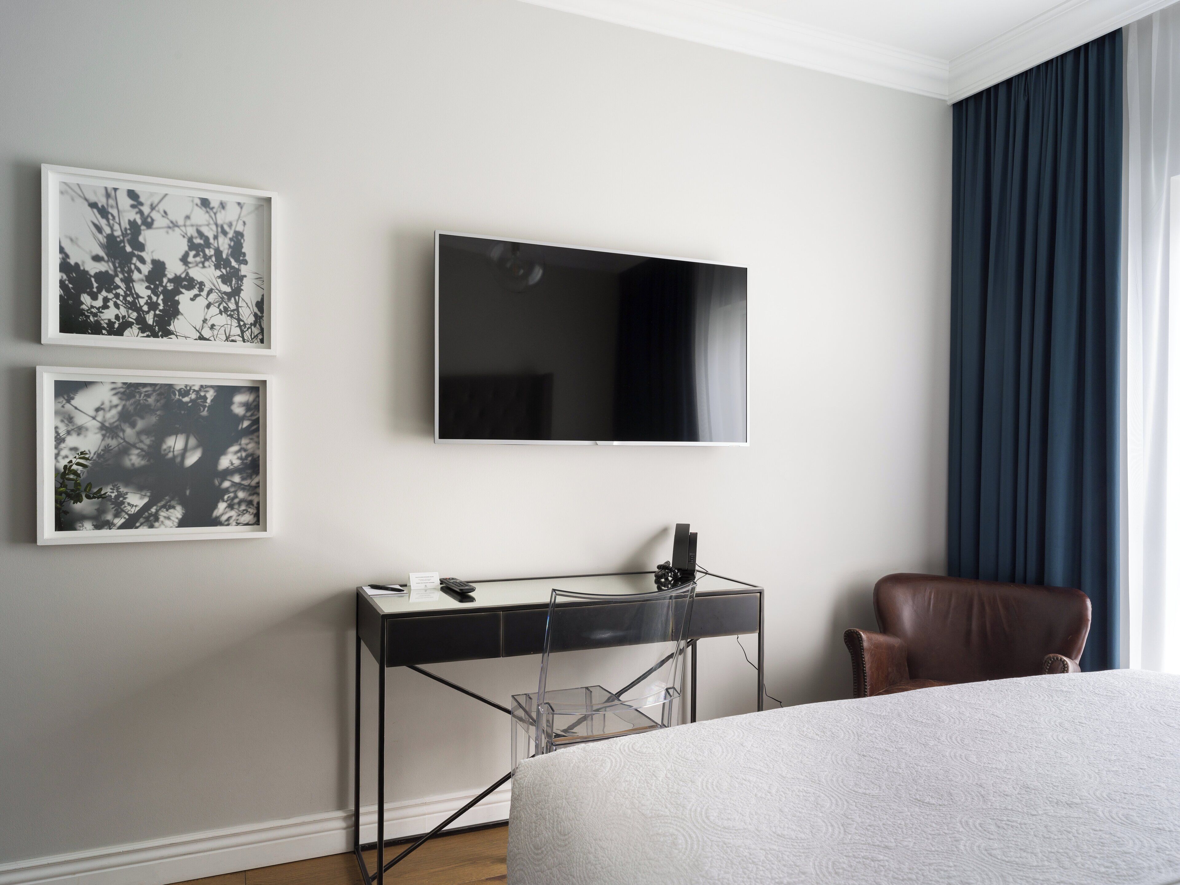 Habitación de hotel con cama, escritorio con computadora, televisor y dos cuadros en la pared.