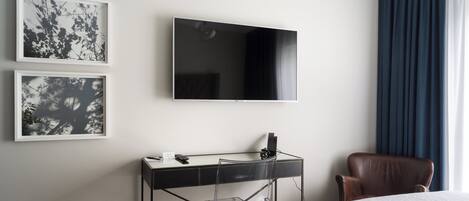 Habitación de hotel con cama, escritorio con computadora, televisor y dos cuadros en la pared.