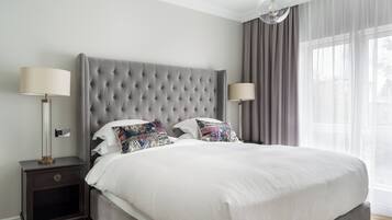 A neatly made bed with a grey upholstered headboard, two bedside lamps, and a nightstand with a drawer.