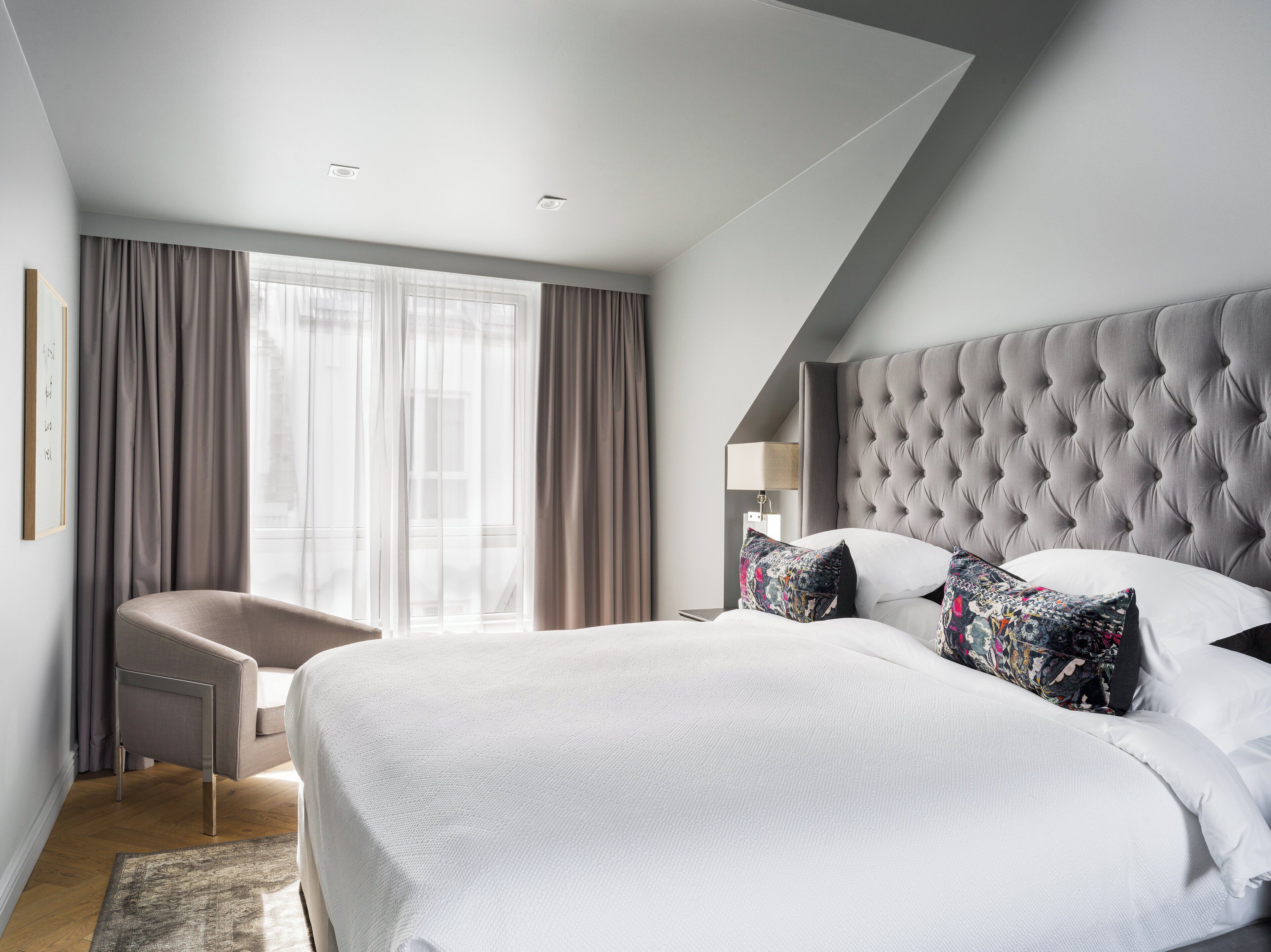 A modern hotel room with a large bed, a chair, and a window with curtains.