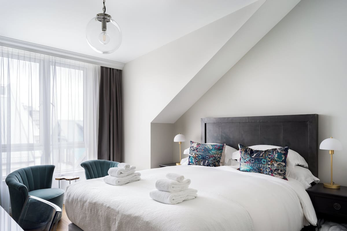 Une chambre d’hôtel moderne dotée d’un grand lit, de deux tables de chevet, d’un bureau, d’une chaise et d’une grande fenêtre avec des rideaux.