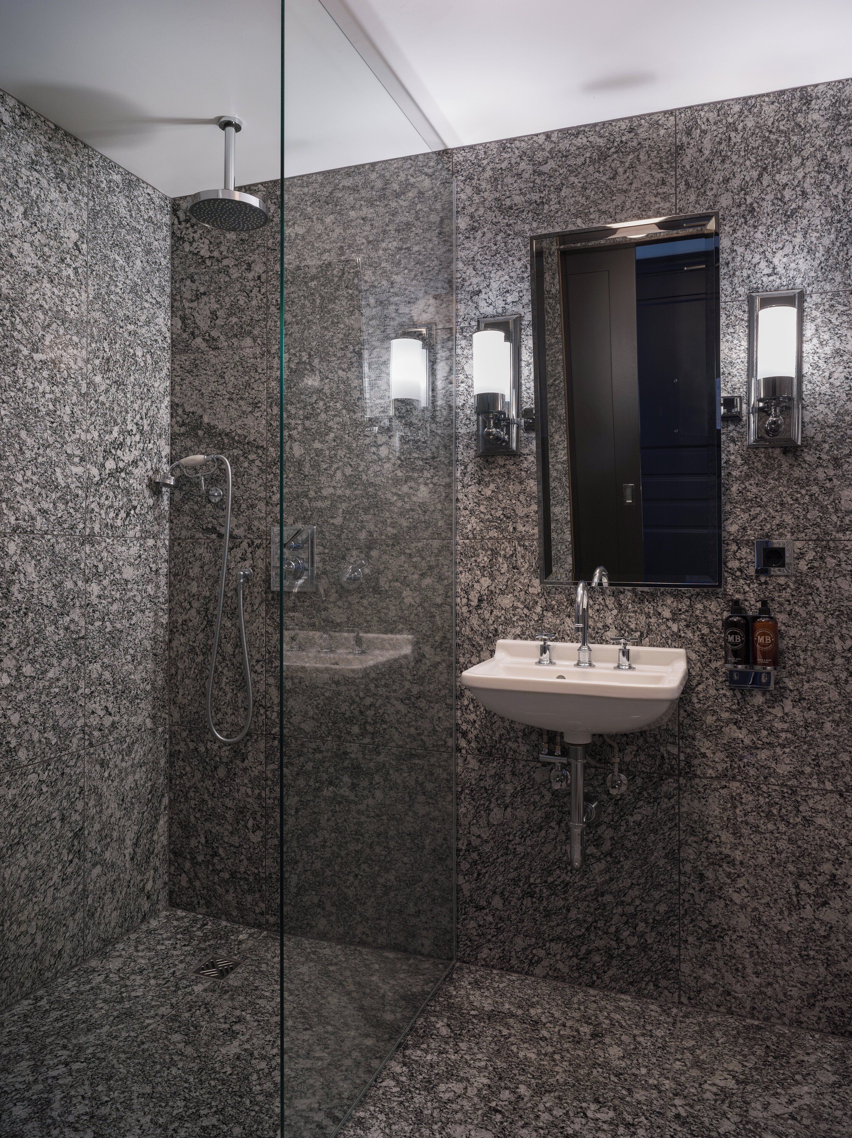 A modern bathroom with a glass-enclosed shower, a sink with a mirror above it, and granite walls.