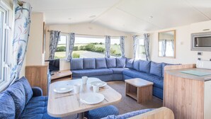 Interior compacto de una caravana con sofá modular, una mesa de comedor y una kitchenette.
