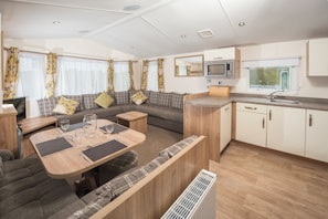 Un espacio habitable compacto con comedor, sofá, kitchenette y un televisor pequeño.