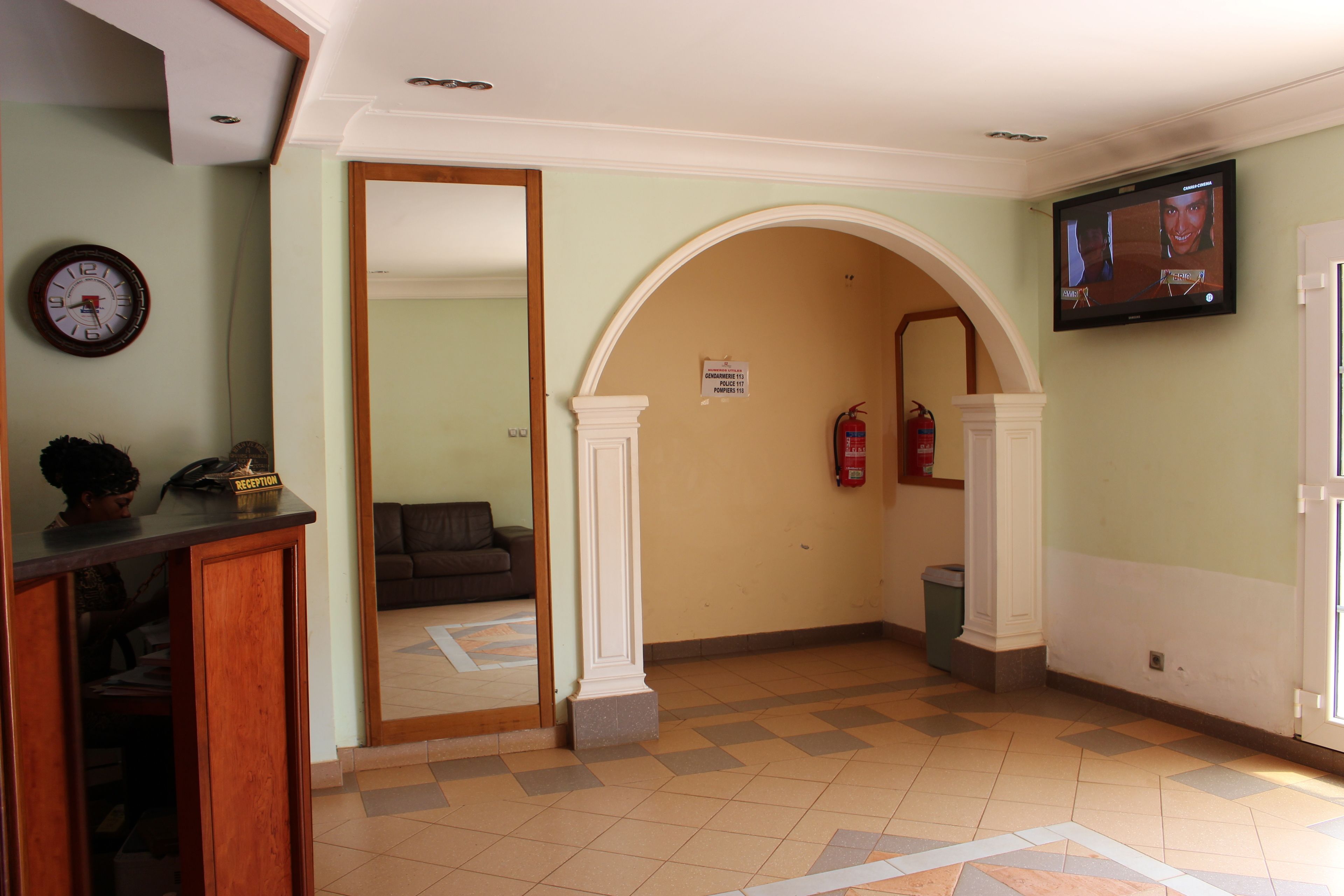 Zona de recepción con mostrador, un reloj, un televisor y un extintor.