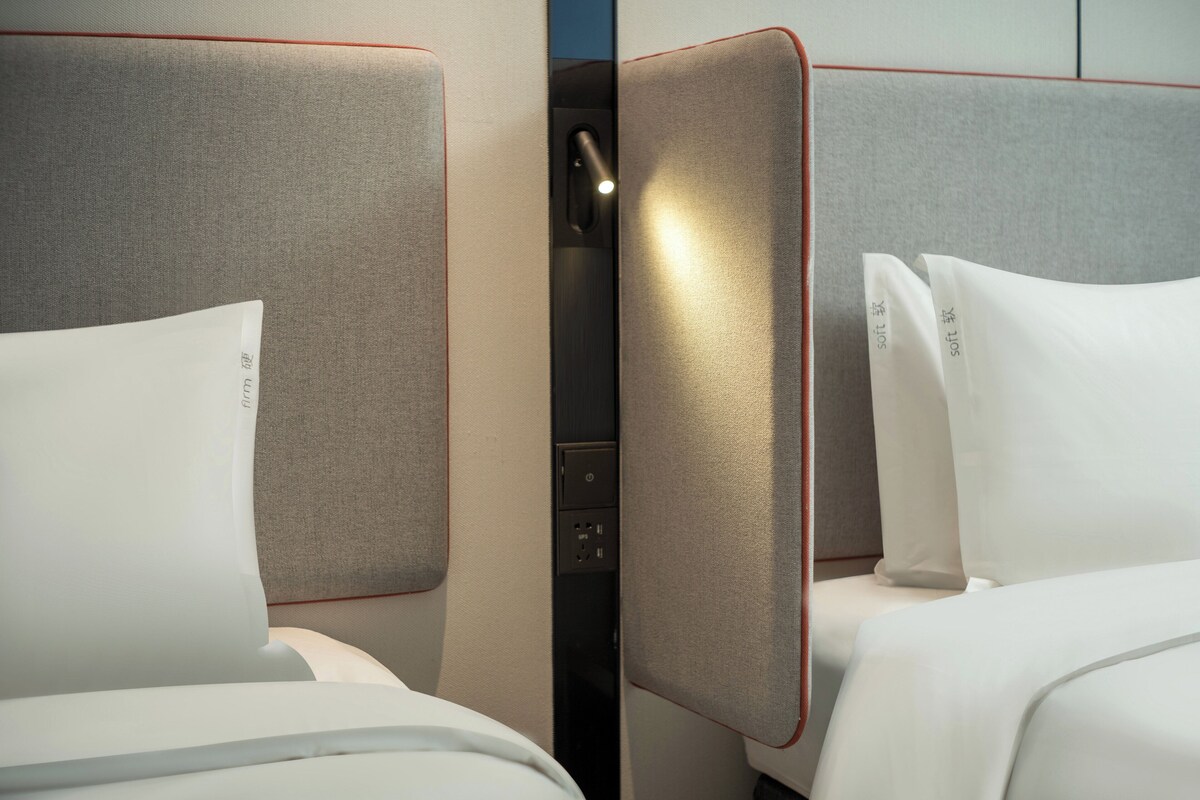 A hotel room with two beds, each with a grey headboard and white bedding.