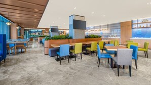 Moderni ravintola, jossa on monipuoliset istumapaikkavaihtoehdot, kuten erillisiä istuinalueita ja pöytiä, keskeinen baarialue sekä näkymä kaupunkimaisemaan.