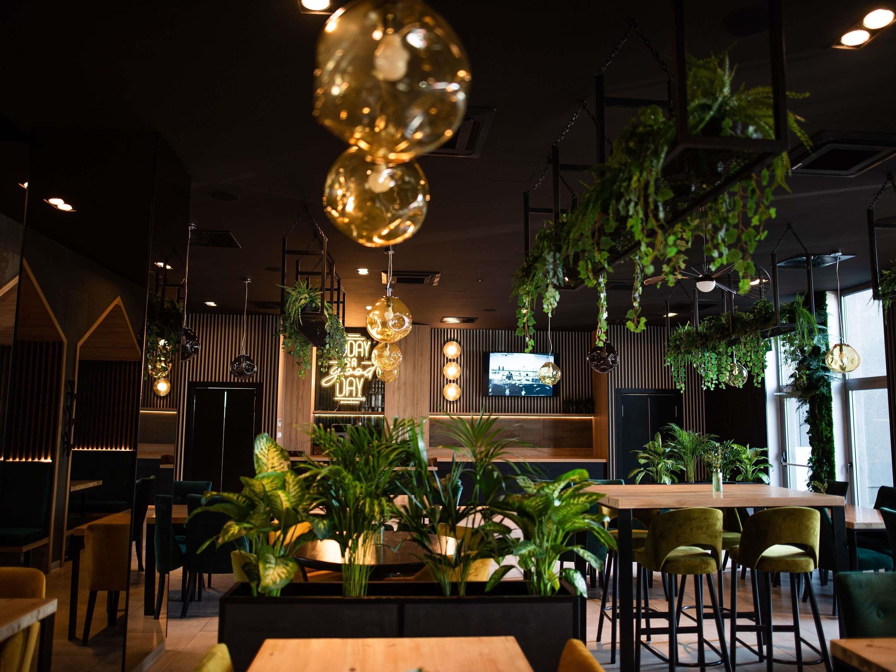 Un intérieur de restaurant moderne avec des luminaires sphériques suspendus, des tables en bois et des plantes vertes.