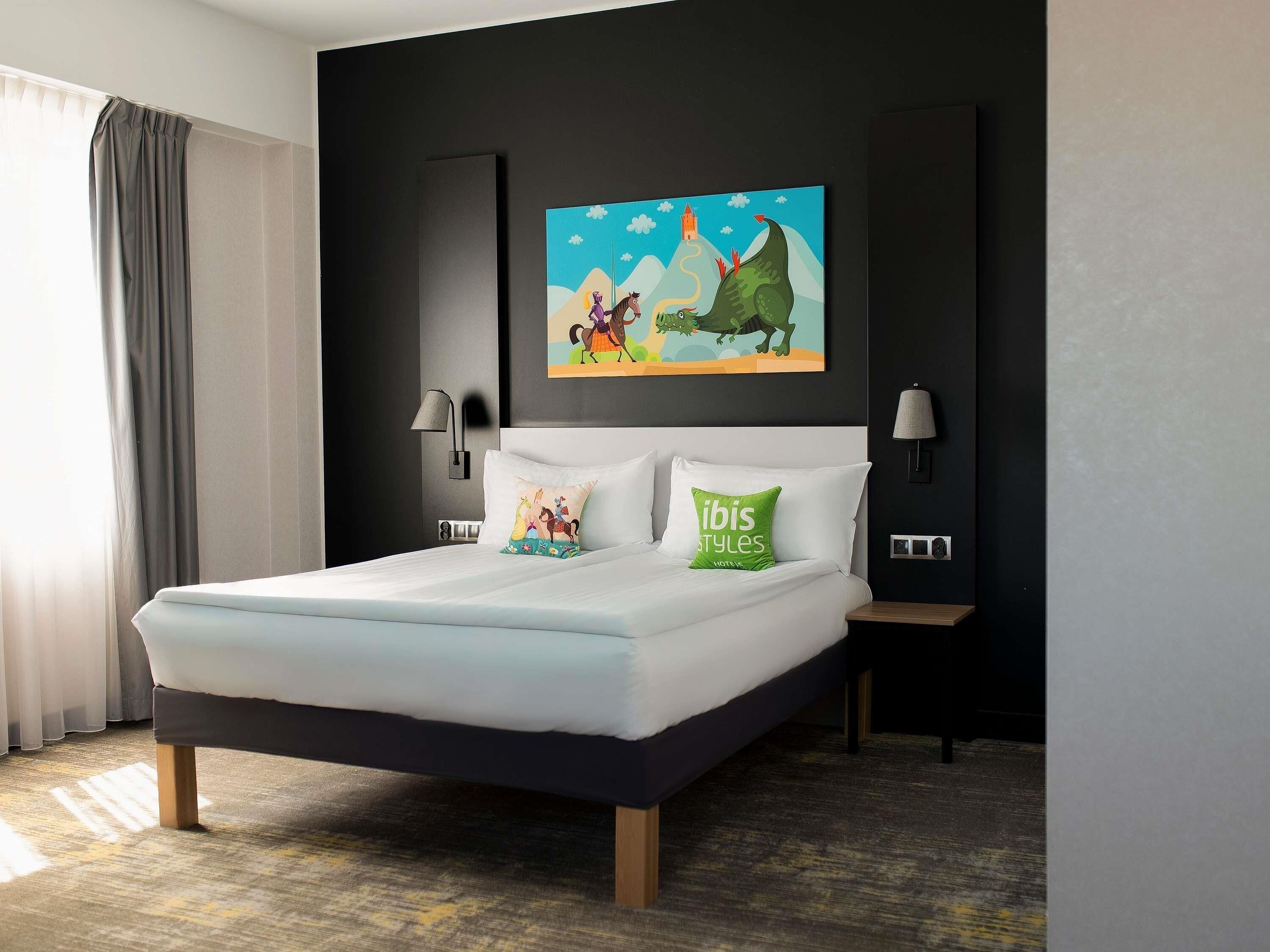 Ein modernes Hotelzimmer mit einem großen Bett, zwei Nachttischlampen, einem Bild an der Wand und einem Fenster mit Vorhängen.