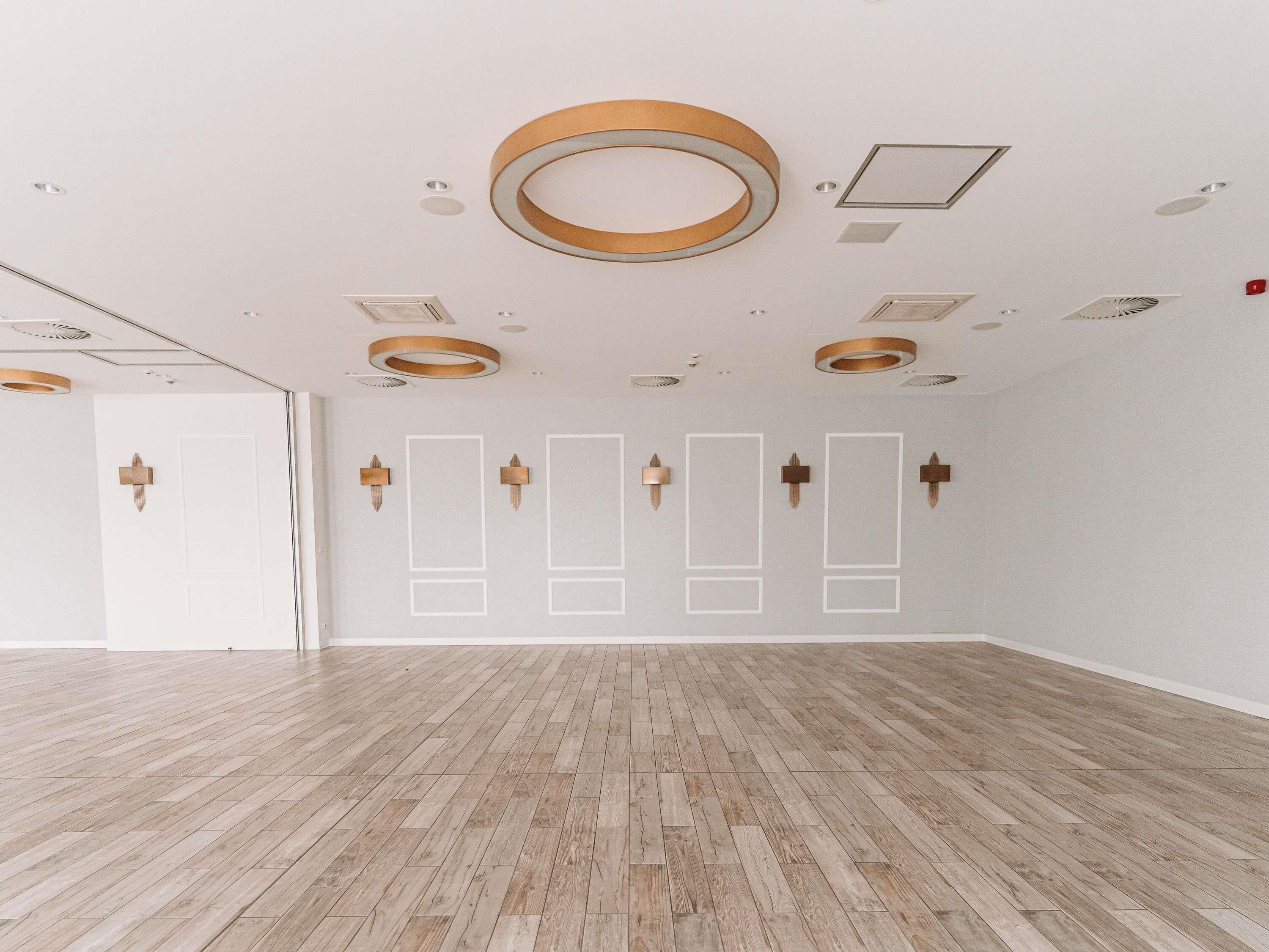 A spacious room with wooden flooring, recessed ceiling lights, and a white door.