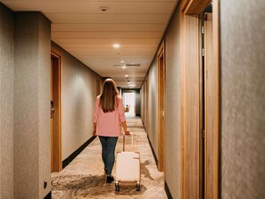 Ein Hotelgang mit Holztüren, einem gemusterten Teppich und einer Person, die einen Koffer zieht.