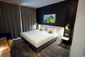 Ett hotellrum med en stor säng, ett skrivbord, en stol och en tavla på väggen.