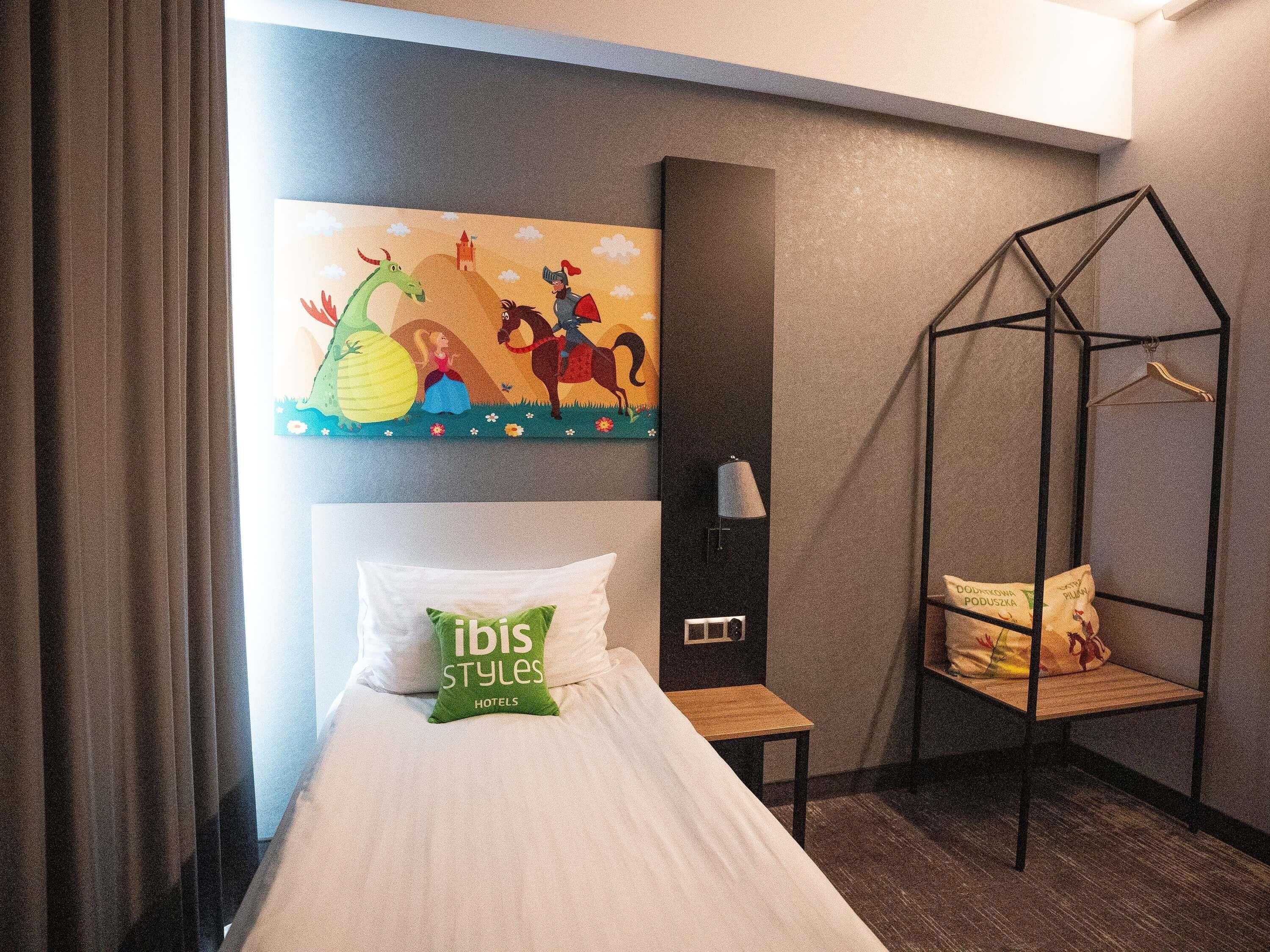 Une chambre d’hôtel avec un lit, un fauteuil suspendu, un tableau mural et un coussin orné du texte « ibis styles hotels ».
