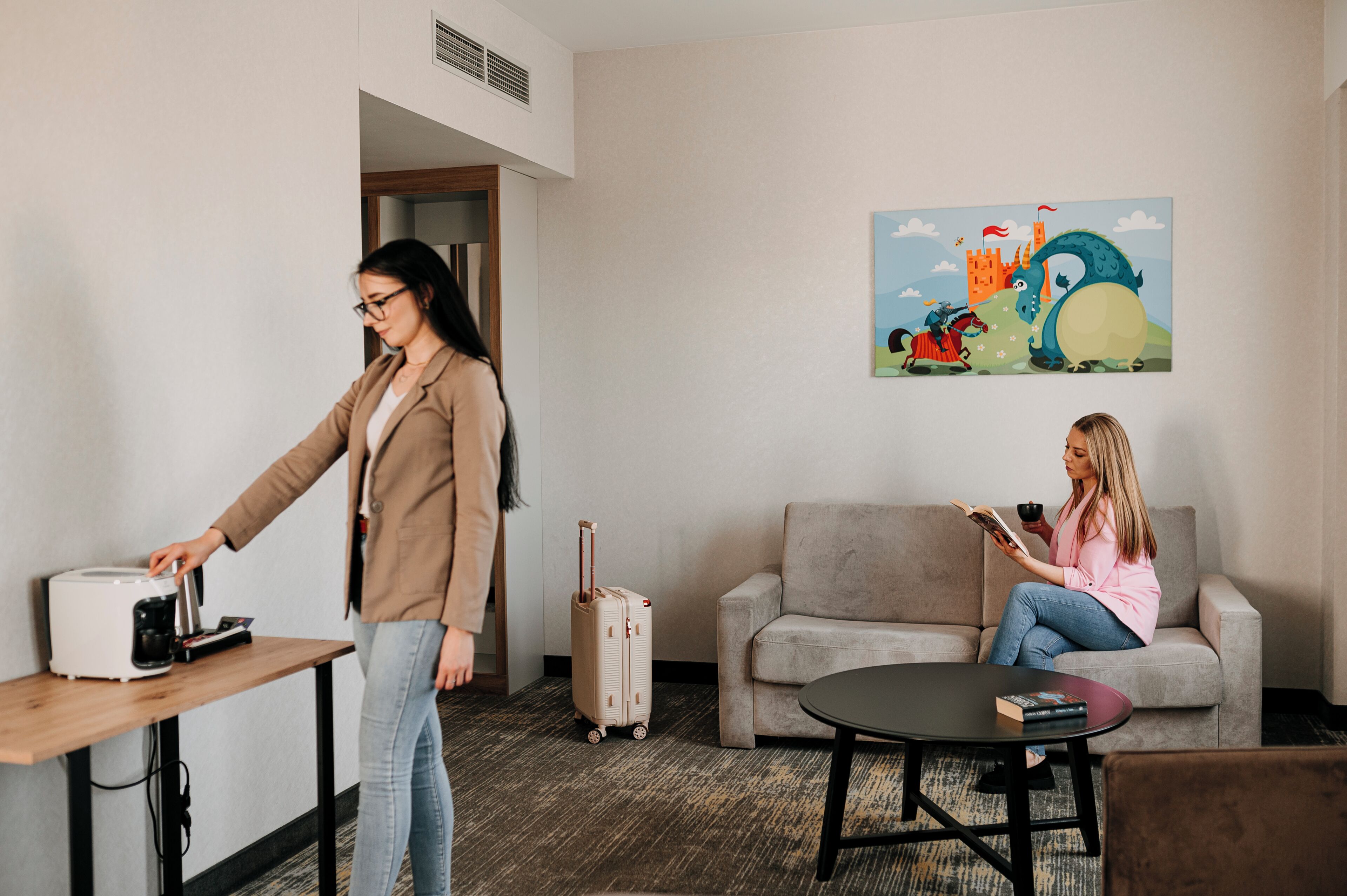 A room with a kitchenette, a sofa, a coffee table, and a painting on the wall.