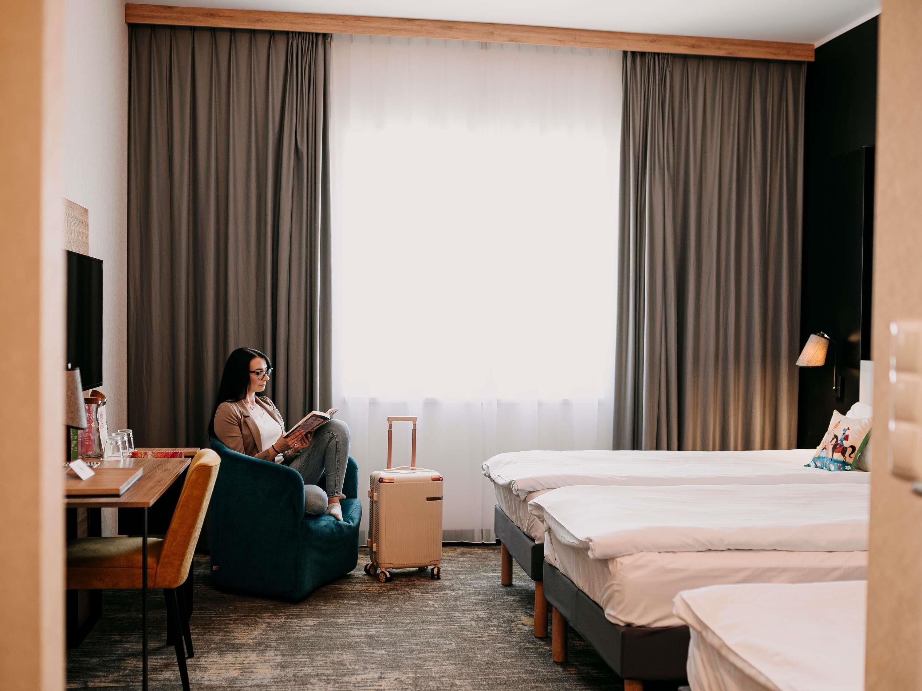 Una habitación de hotel con cama, escritorio, silla, maleta y televisor.
