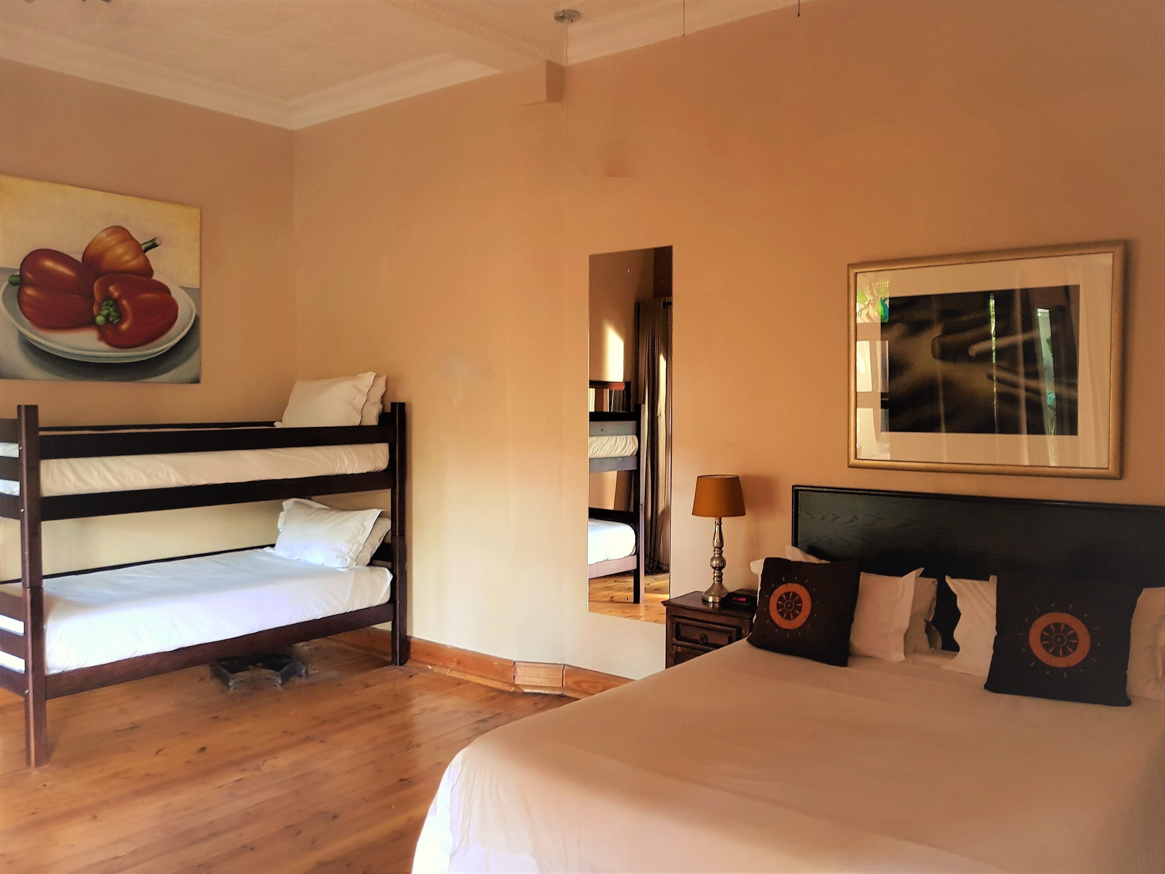 Habitación de hotel con literas, una cama grande, un cuadro de fruta, un espejo y un marco con una fotografía en la pared.