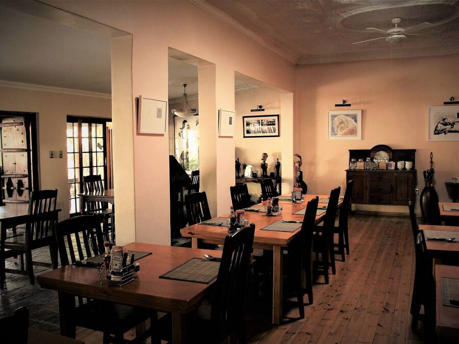 A dining area with wooden tables and chairs, a ceiling fan, and framed pictures on the walls.