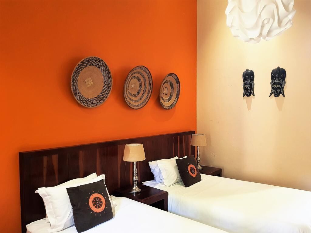 Une chambre d’hôtel avec deux lits, une tête de lit en bois et un mur décoré d’assiettes et de masques.