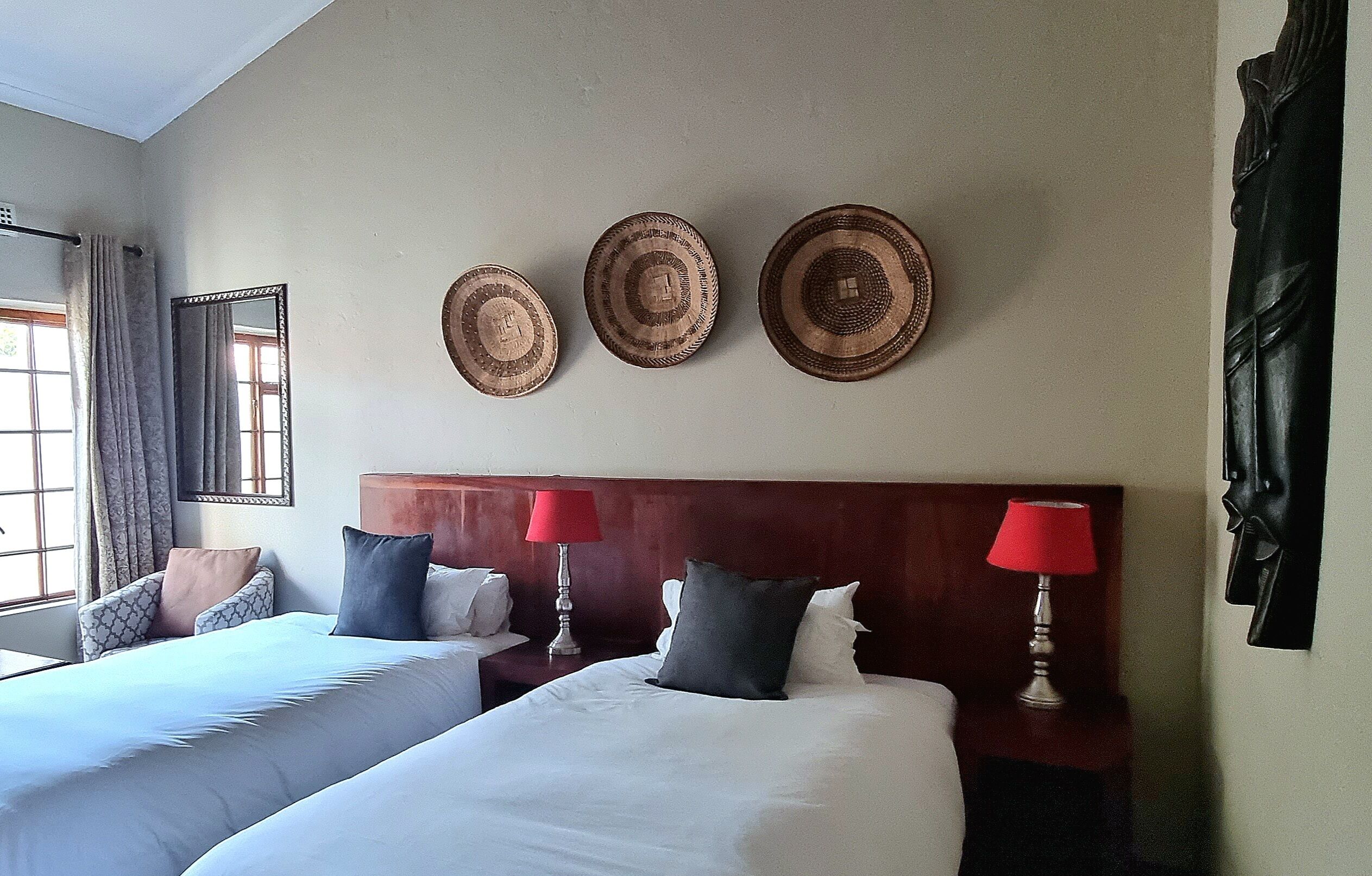 Habitación de hotel con dos camas, cabecera de madera, espejo y tres platos decorativos colgados en la pared.