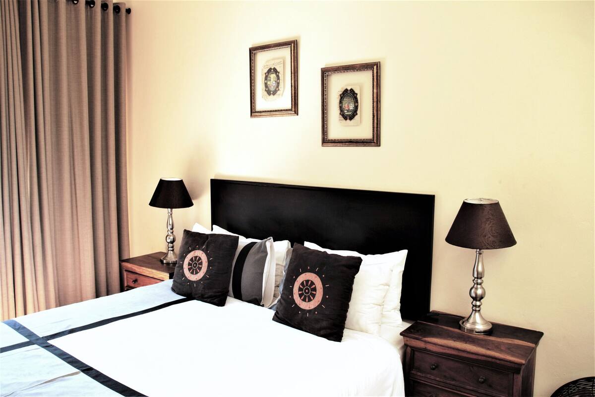 A neatly made bed with a black headboard, two bedside tables with lamps, and two framed pictures on the wall.