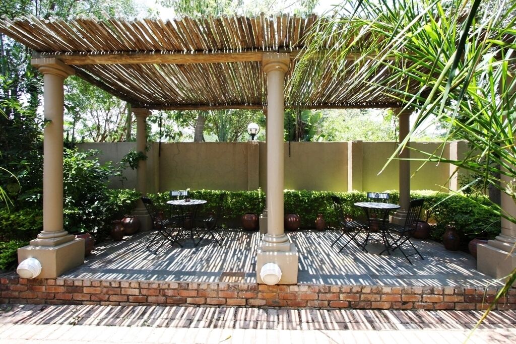 Un espacio al aire libre cubierto con mesas y sillas, rodeado de follaje y un muro de ladrillo.