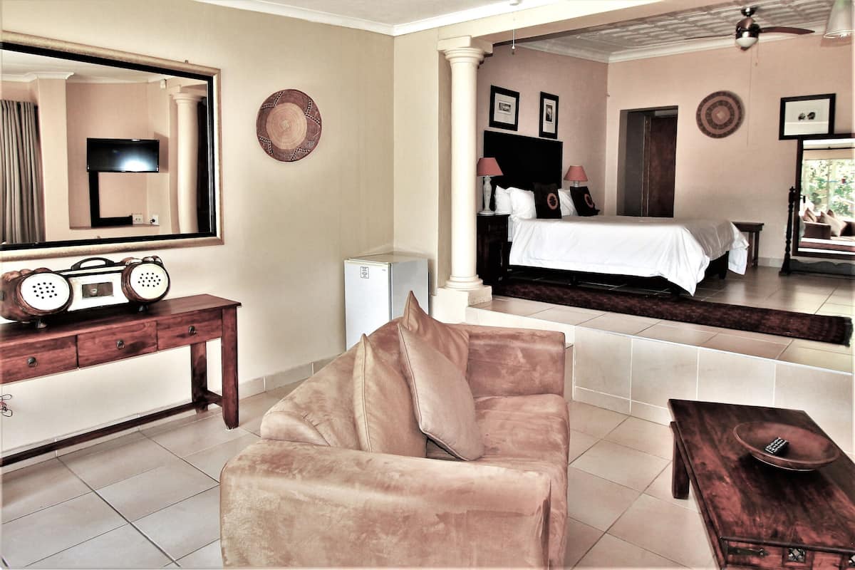 A hotel room with a bed, a sofa, a desk with a radio, a mirror, and a television.