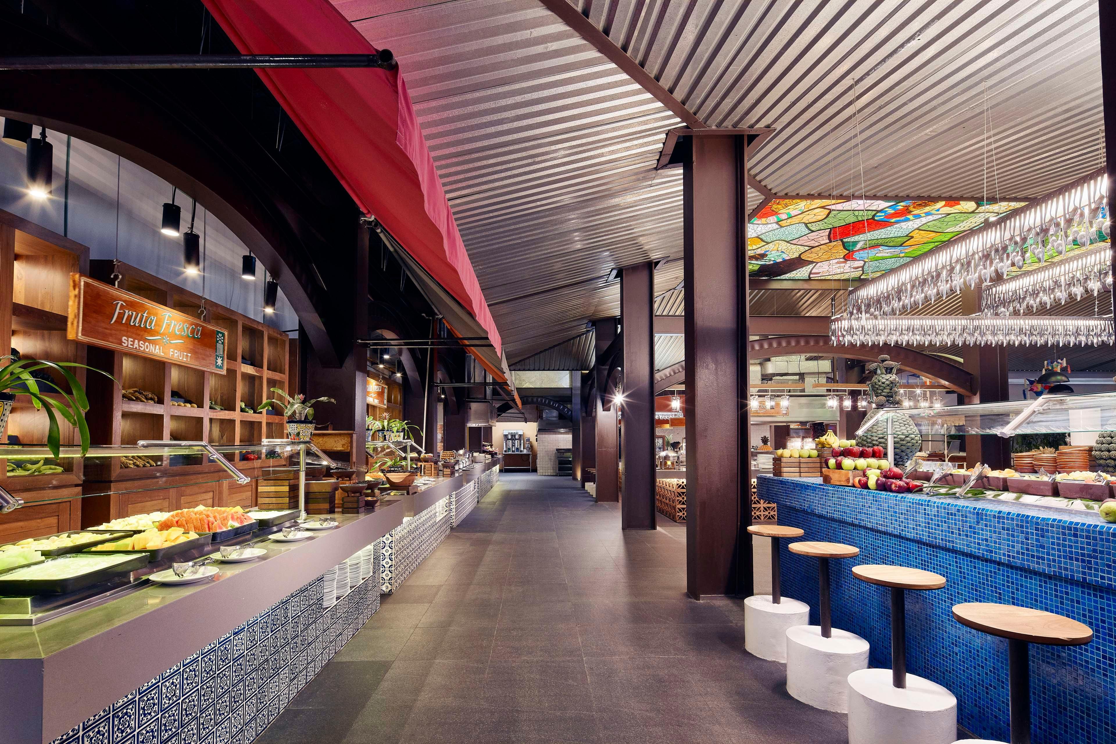 A buffet area with a variety of food options, a seating area with stools, and a colorful stained glass ceiling.