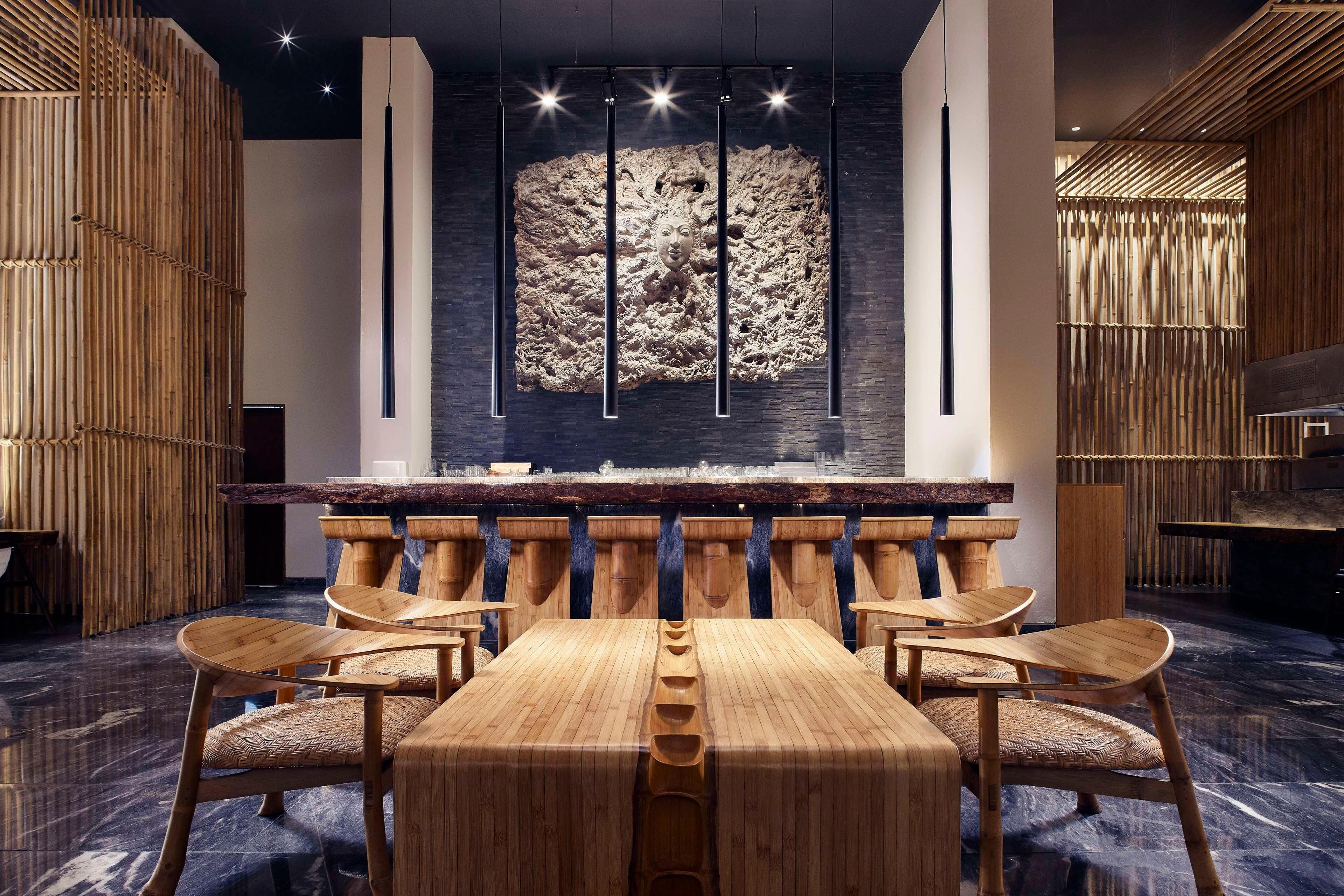 A modern interior with a central wooden table and chairs, a large wall art piece, and bamboo decor.
