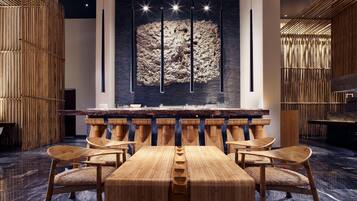A modern interior with a central wooden table and chairs, a large wall art piece, and bamboo decor.