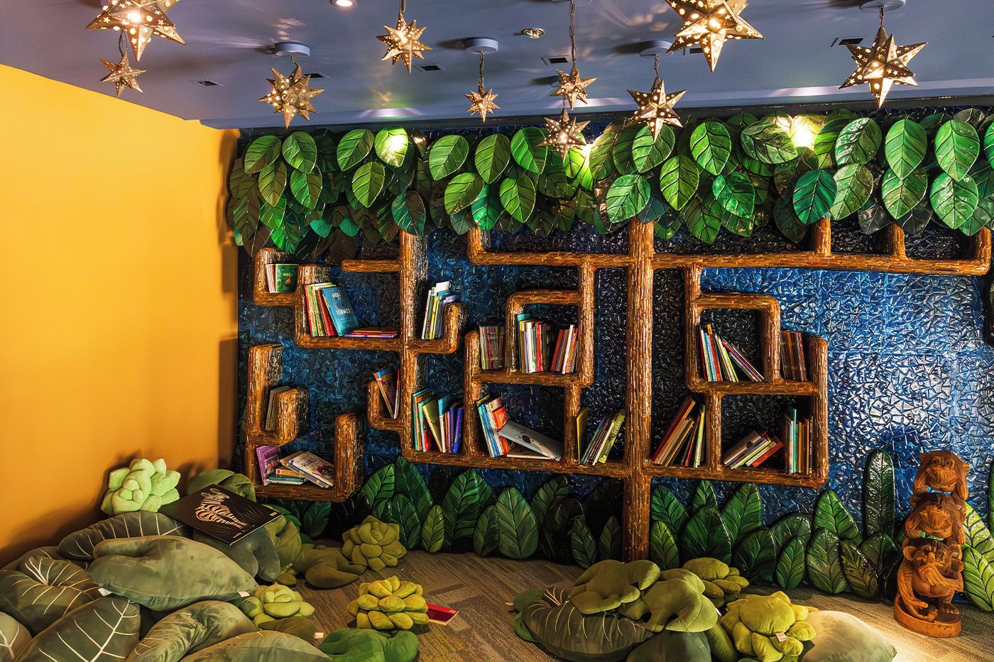 A room with a bookshelf integrated into a wall with a leafy backdrop, a small statue, and a ceiling with star-shaped lights.