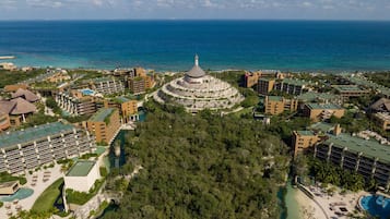 An aerial view of a resort with multiple buildings, a central circular structure, and a beach area.