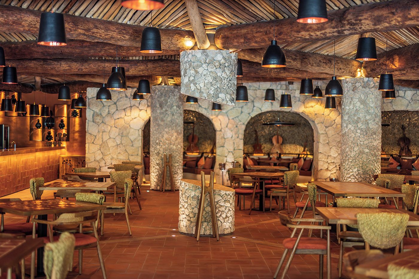 A restaurant interior with stone pillars, wooden tables, and hanging black pendant lights.