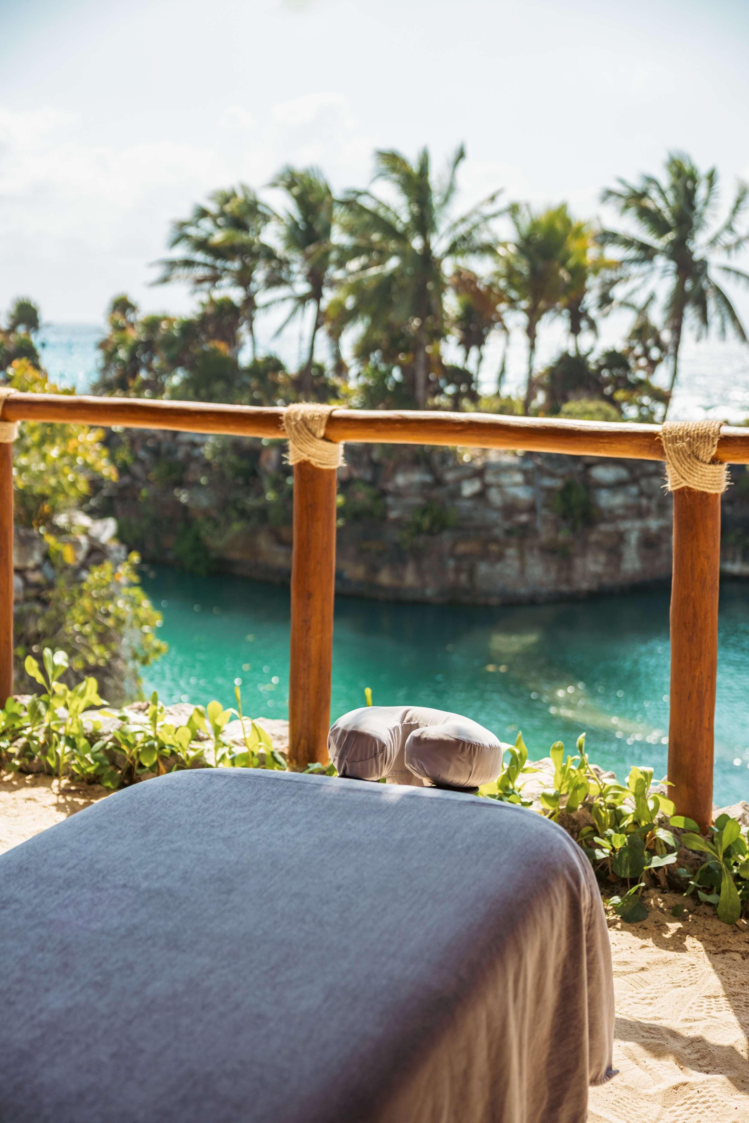 A beachside spa area with a wooden railing, a stone bench, and a view of the ocean and palm trees.