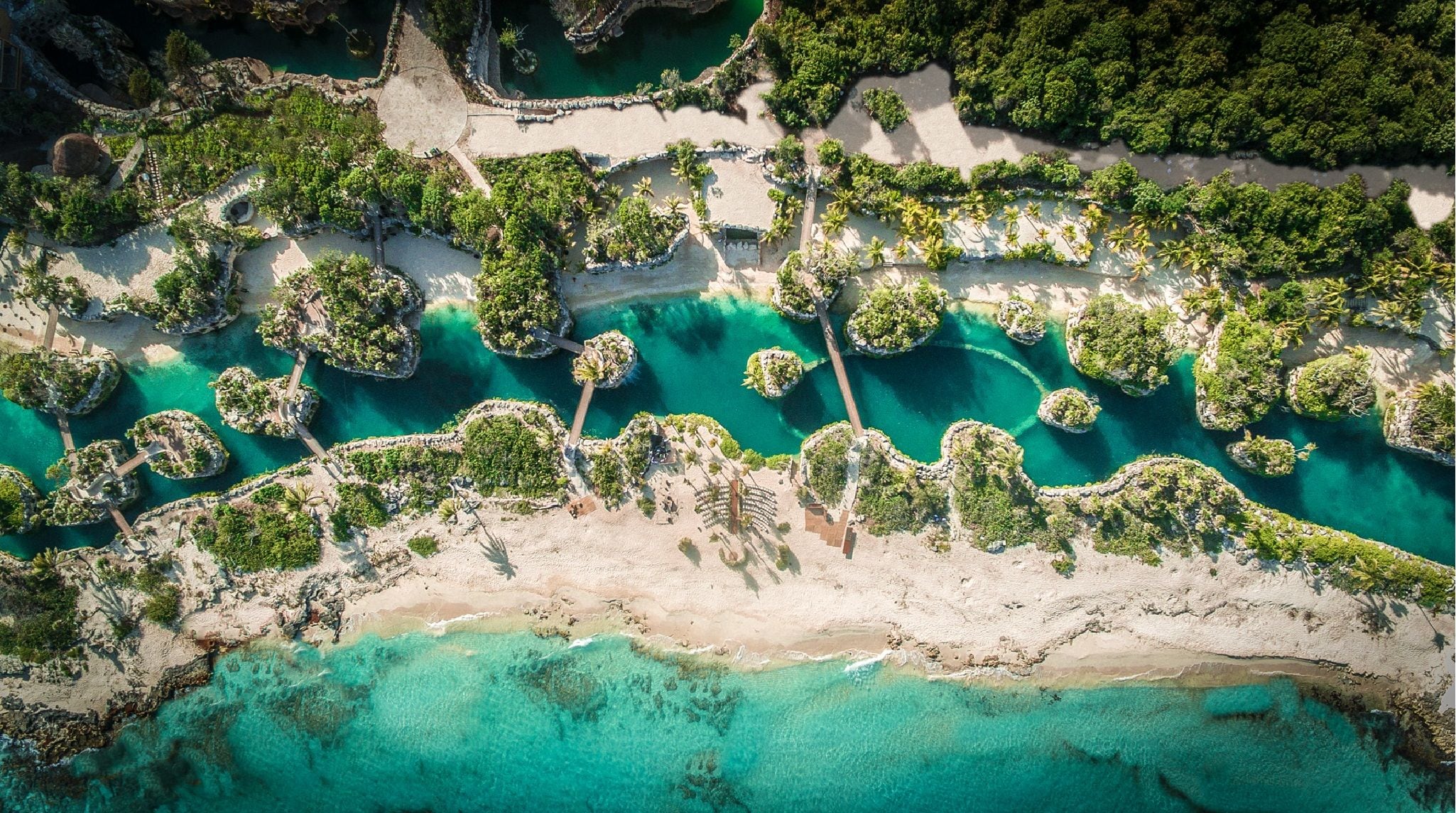 An aerial view of a coastal resort with clear turquoise waters, sandy beaches, and lush greenery.