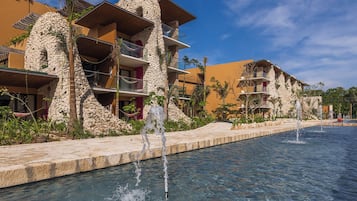 A resort with multiple-story buildings, a swimming pool with water fountains, and tropical landscaping.