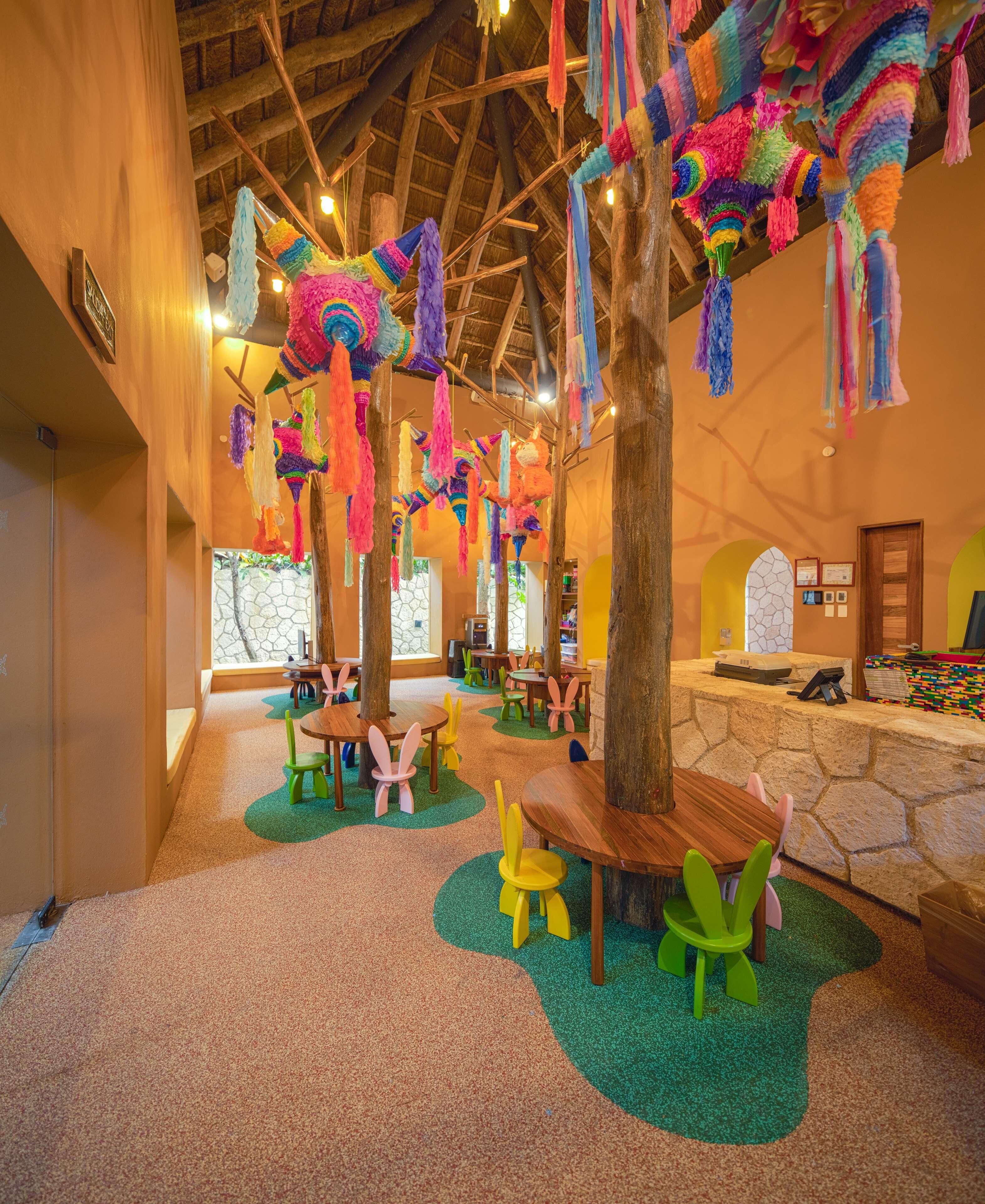 A children's play area with colorful hanging decorations, wooden tables, and chairs.