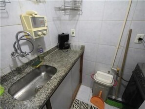 Uma cozinha pequena com bancada de granito, pia de aço inoxidável, cafeteira e um rodo.