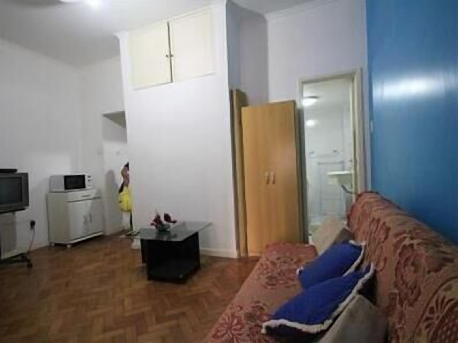 A small, compact living space with a sofa, a television, a microwave, and a cabinet.