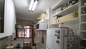 A compact kitchen with a refrigerator, microwave, and shelves with various items. - GoHouse Dulcidio 307 (Rio de Janeiro)