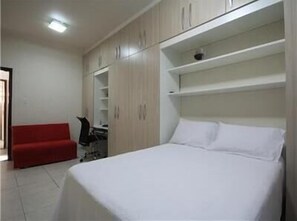 A bedroom with a bed, a red chair, and a wardrobe with multiple shelves. - GoHouse Dutra 804 (Rio de Janeiro)