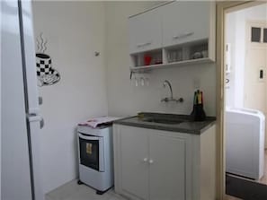 Uma pequena cozinha compacta com pia, micro-ondas e armário sobre a bancada.