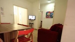 A dining area with a wooden table and red chairs, a red sofa, and a television on the wall. - GoHouse Copacabana 901 (Rio de Janeiro)