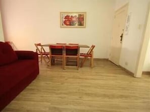 Um quarto com uma mesa de jantar de madeira e cadeiras, um sofá vermelho e um quadro na parede.