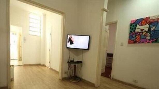 A hallway with a television mounted on the wall, wooden flooring, and a colorful painting on the wall. - GoHouse Copacabana 901 (Rio de Janeiro)