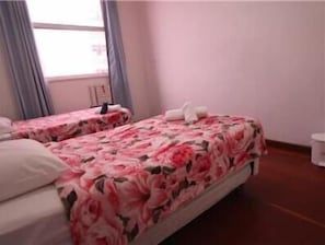 Quarto de hotel com duas camas, cada uma com roupa de cama e almofadas estampadas.