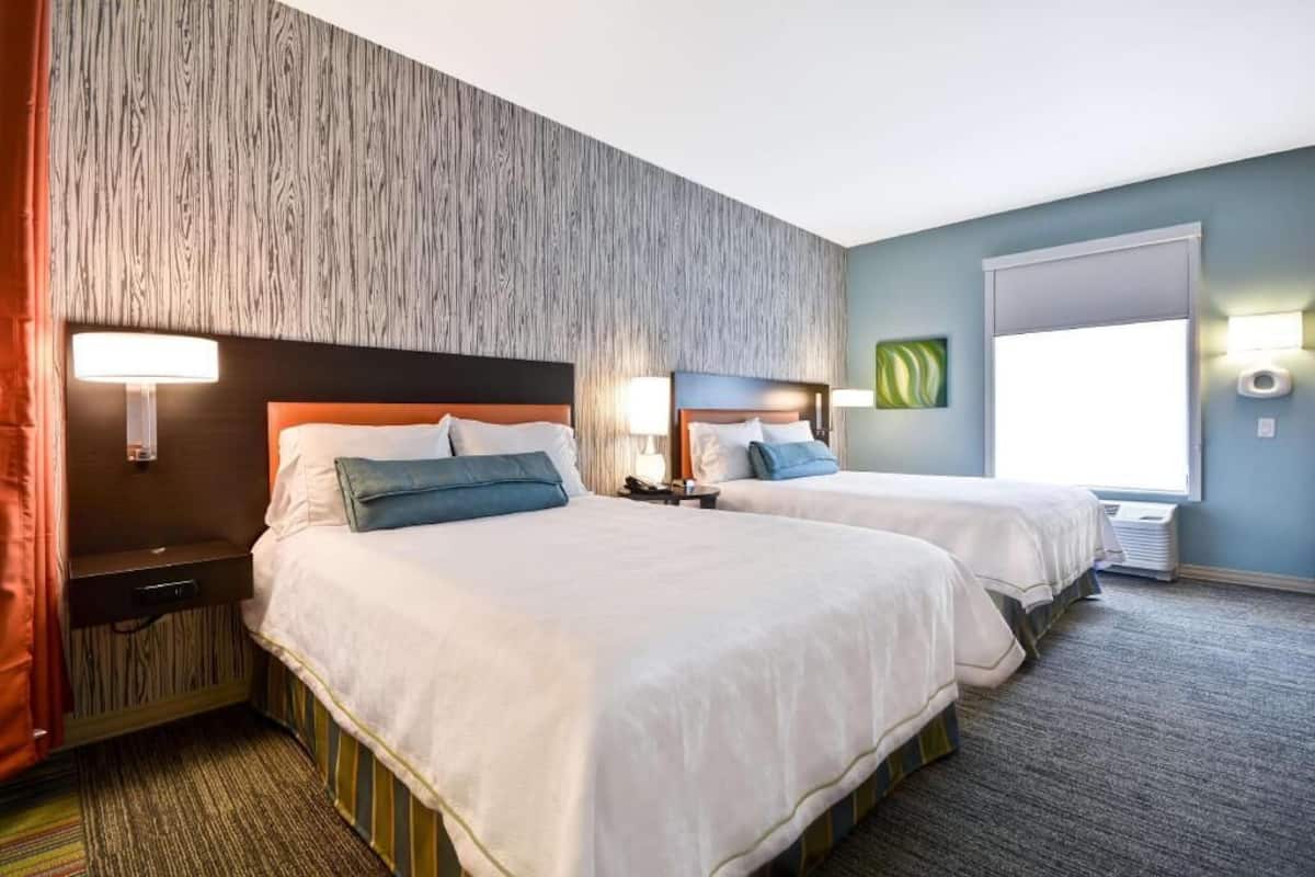 A hotel room with two beds, a wooden accent wall, a large window, and a carpeted floor.