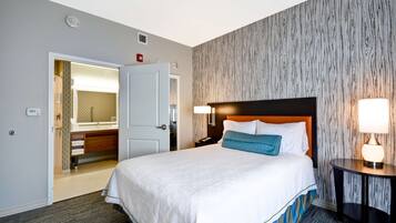 Habitación de hotel con cama, mesita de noche, lámpara, espejo y baño visible a través de una puerta abierta.